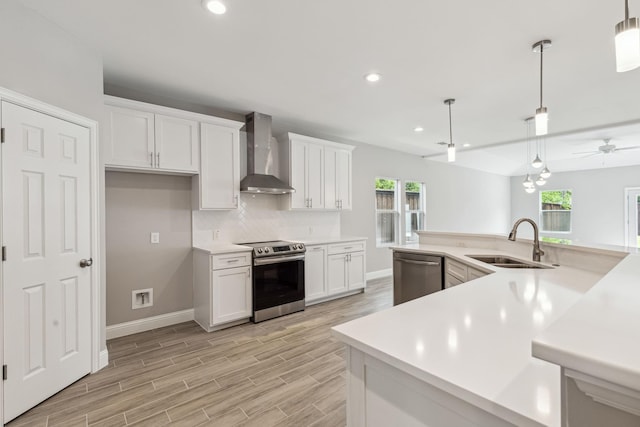 kitchen with appliances with stainless steel finishes, pendant lighting, white cabinetry, sink, and wall chimney exhaust hood