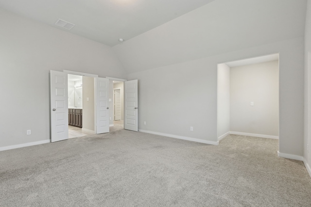 unfurnished bedroom featuring lofted ceiling, ensuite bath, and light colored carpet