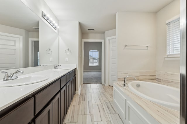 bathroom featuring a bath, visible vents, double vanity, and a sink