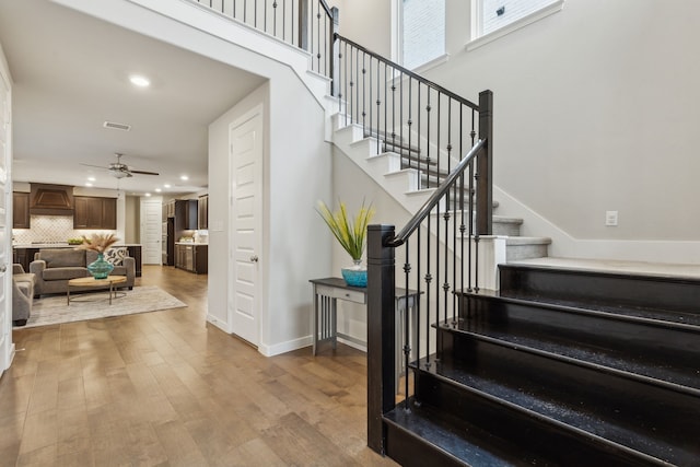 stairway with a towering ceiling, wood-type flooring, and ceiling fan