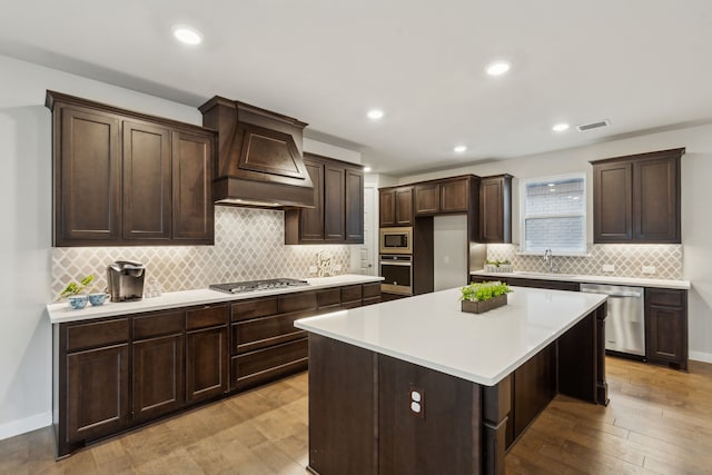 kitchen featuring custom exhaust hood, a center island, light hardwood / wood-style flooring, appliances with stainless steel finishes, and backsplash