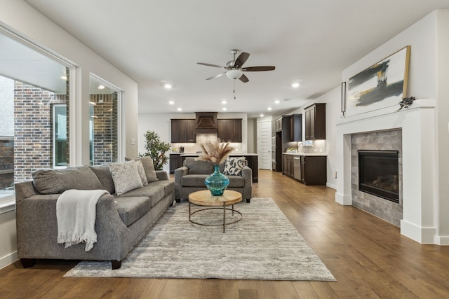 living area with a ceiling fan, a tiled fireplace, dark wood finished floors, recessed lighting, and baseboards