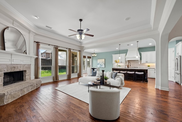 living area with a stone fireplace, visible vents, ornamental molding, and ceiling fan with notable chandelier