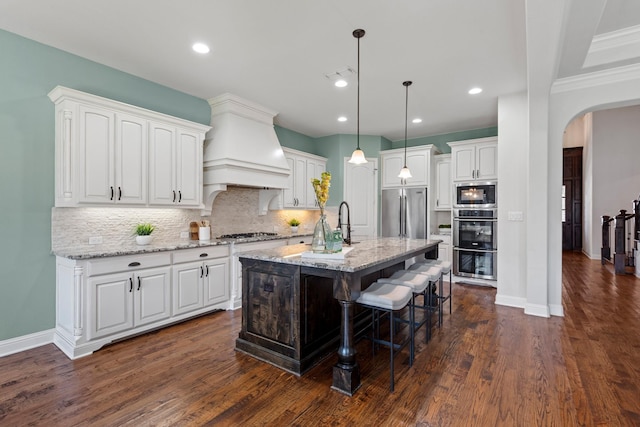 kitchen with premium range hood, arched walkways, white cabinets, and stainless steel appliances