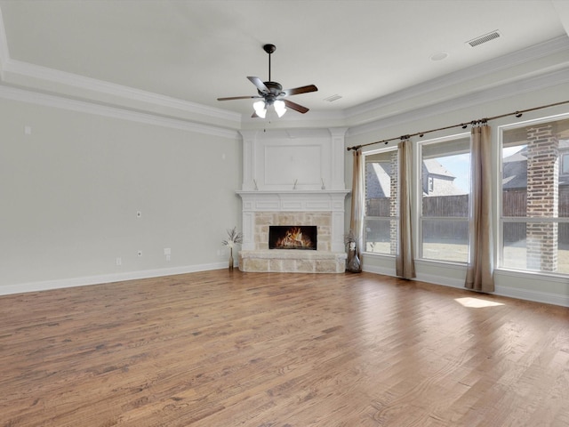 unfurnished living room featuring crown molding, ceiling fan, wood-type flooring, and a stone fireplace