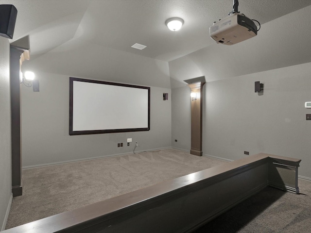 carpeted home theater room featuring lofted ceiling, ornate columns, visible vents, and baseboards