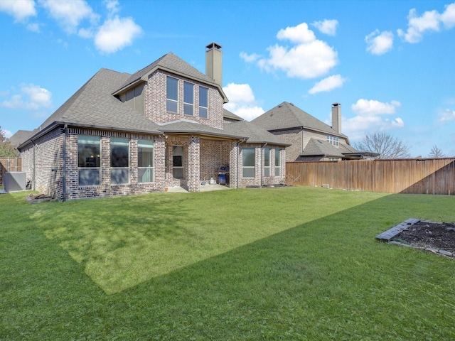 back of house featuring a lawn, fence private yard, roof with shingles, and brick siding