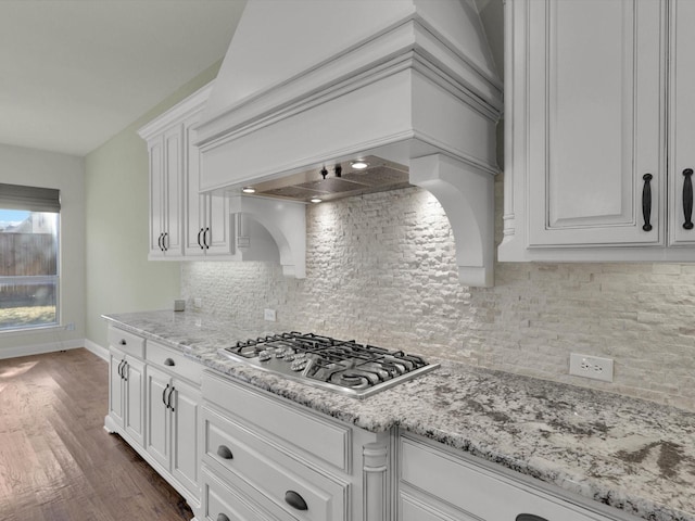 kitchen featuring dark wood-type flooring, stainless steel gas cooktop, custom exhaust hood, white cabinetry, and light stone countertops