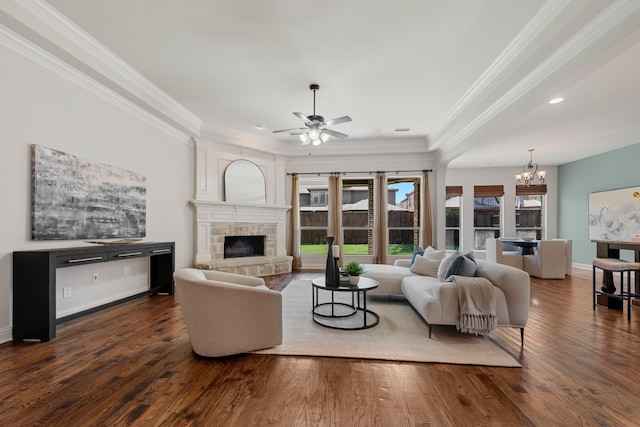 living area with crown molding, wood finished floors, a stone fireplace, and ceiling fan with notable chandelier