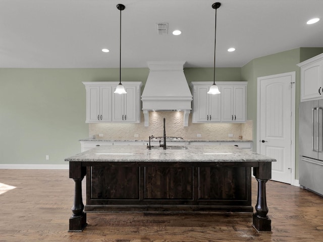 kitchen with premium range hood, hanging light fixtures, a center island with sink, stainless steel appliances, and white cabinets