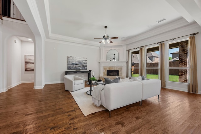 living area with crown molding, wood finished floors, a fireplace with raised hearth, ceiling fan, and visible vents