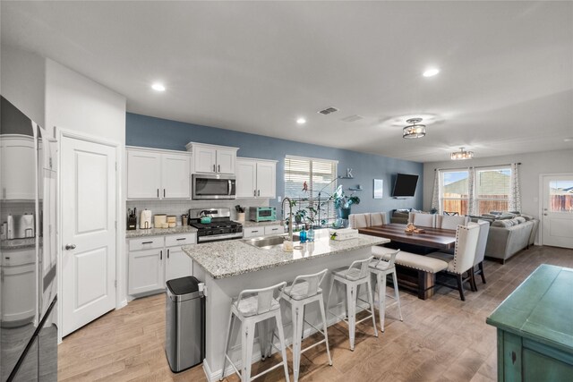 kitchen with a breakfast bar, sink, white cabinetry, appliances with stainless steel finishes, and a kitchen island with sink