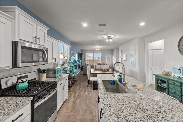 kitchen featuring sink, light hardwood / wood-style flooring, stainless steel appliances, light stone counters, and white cabinets