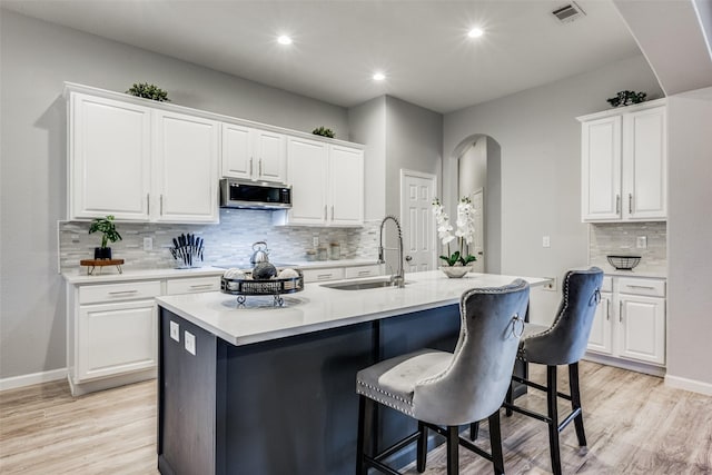 kitchen featuring sink, a breakfast bar area, white cabinets, a kitchen island with sink, and light wood-type flooring