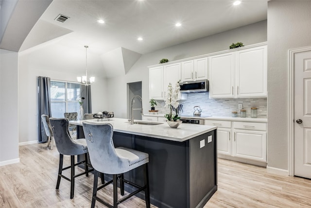 kitchen with vaulted ceiling, sink, white cabinets, backsplash, and a center island with sink