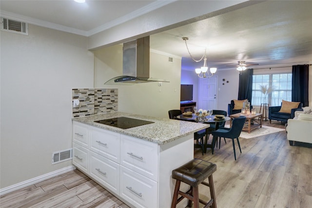 kitchen with pendant lighting, light stone counters, island range hood, white cabinets, and black electric cooktop