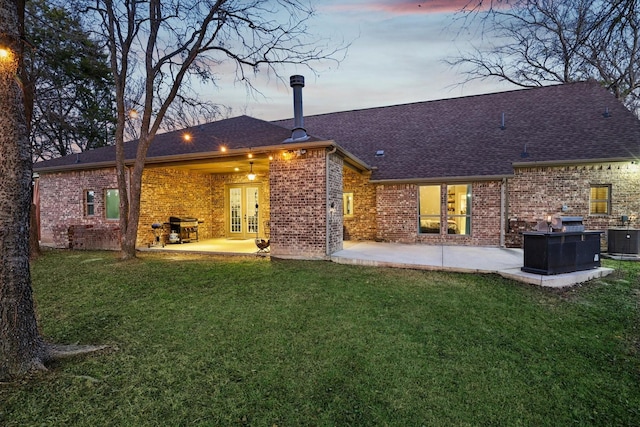 back house at dusk featuring a patio, a lawn, central AC unit, and french doors