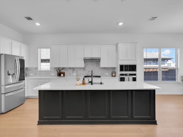 kitchen with tasteful backsplash, appliances with stainless steel finishes, an island with sink, and white cabinets