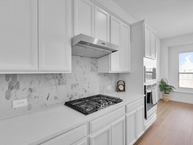 kitchen featuring stainless steel appliances, white cabinets, backsplash, and light hardwood / wood-style flooring