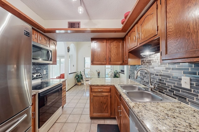 kitchen featuring light tile patterned flooring, sink, kitchen peninsula, stainless steel appliances, and a textured ceiling