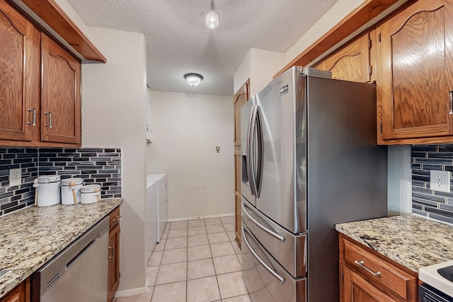 kitchen featuring appliances with stainless steel finishes, independent washer and dryer, light stone countertops, light tile patterned flooring, and decorative backsplash