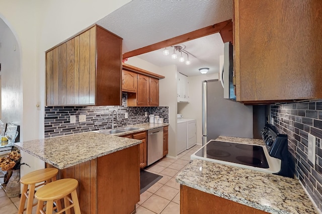 kitchen featuring sink, a breakfast bar area, washer and dryer, light tile patterned floors, and appliances with stainless steel finishes