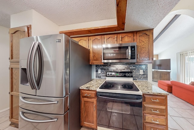 kitchen with appliances with stainless steel finishes, tasteful backsplash, light stone counters, a textured ceiling, and light tile patterned flooring