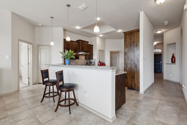 kitchen with a kitchen island, decorative light fixtures, decorative backsplash, dark brown cabinetry, and light stone counters