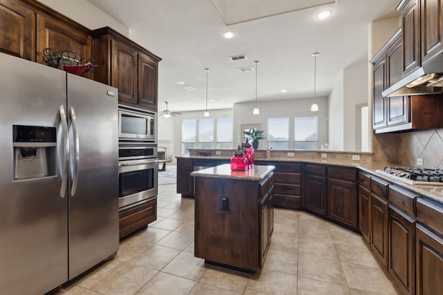 kitchen with dark brown cabinets, kitchen peninsula, pendant lighting, stainless steel appliances, and decorative backsplash