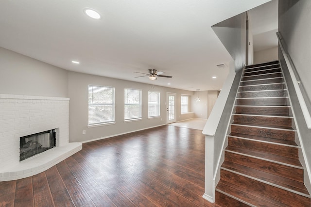 staircase featuring ceiling fan, hardwood / wood-style floors, and a brick fireplace