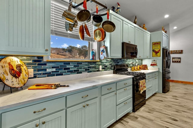 kitchen with light stone counters, green cabinetry, black appliances, light hardwood / wood-style floors, and backsplash