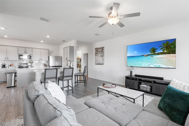 living room featuring ceiling fan, sink, and light hardwood / wood-style floors