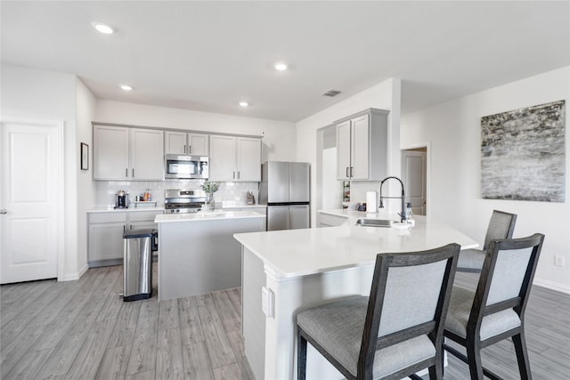 kitchen with stainless steel appliances, a kitchen bar, sink, and gray cabinetry