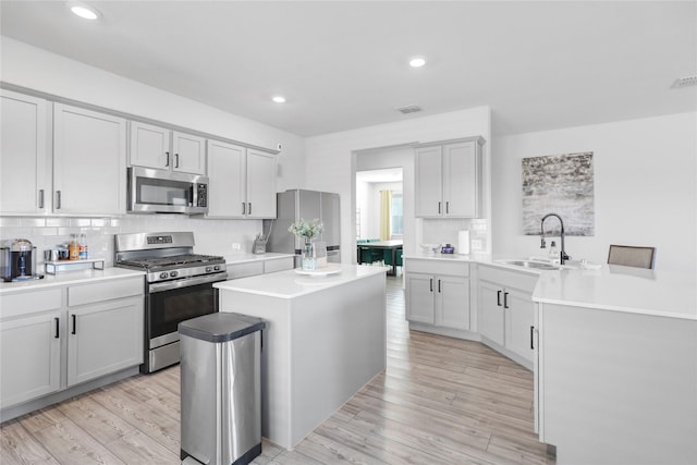 kitchen with sink, light hardwood / wood-style flooring, backsplash, stainless steel appliances, and a center island