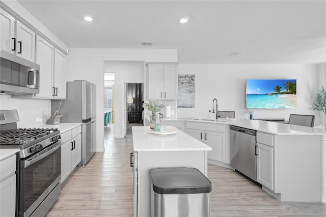 kitchen with sink, light wood-type flooring, a kitchen island, stainless steel appliances, and white cabinets