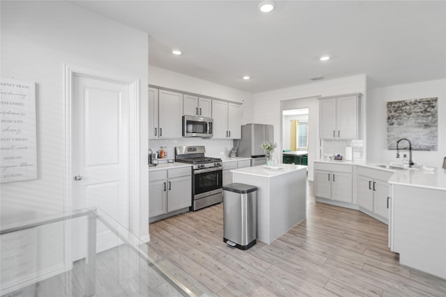 kitchen featuring sink, light hardwood / wood-style flooring, appliances with stainless steel finishes, backsplash, and a kitchen island