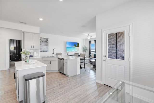 kitchen with stainless steel dishwasher, kitchen peninsula, a kitchen island, and light wood-type flooring