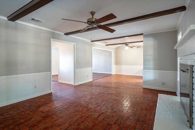 empty room with ceiling fan, ornamental molding, beam ceiling, and a brick fireplace