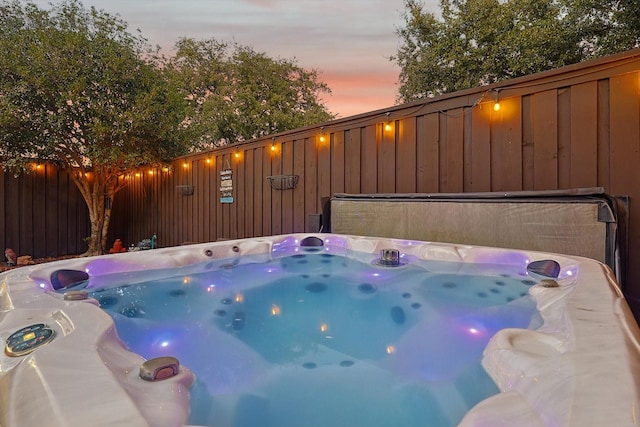 pool at dusk with a hot tub