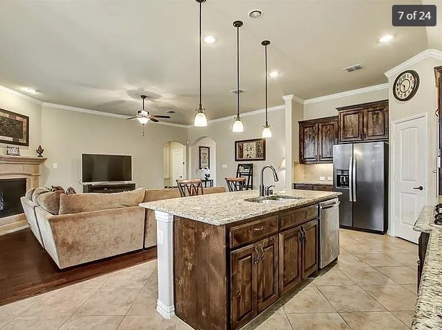 kitchen with pendant lighting, sink, appliances with stainless steel finishes, light stone counters, and a center island with sink