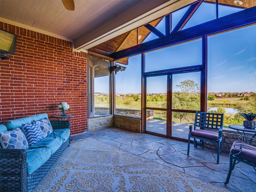 sunroom / solarium featuring vaulted ceiling with beams, ceiling fan, and a water view