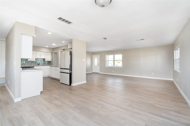 kitchen with tasteful backsplash, light wood-type flooring, white cabinets, and white fridge