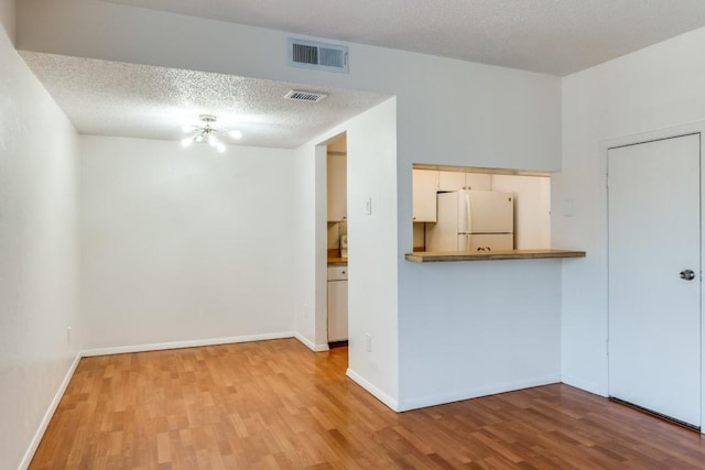 unfurnished room with an inviting chandelier, light hardwood / wood-style floors, and a textured ceiling