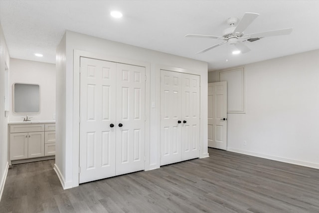 unfurnished bedroom with ensuite bathroom, sink, light wood-type flooring, two closets, and ceiling fan