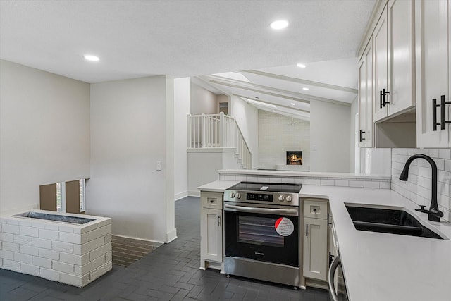 kitchen with sink, electric range, white cabinets, a fireplace, and backsplash