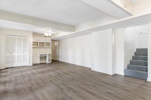 unfurnished living room with ceiling fan, a textured ceiling, built in desk, and wood-type flooring