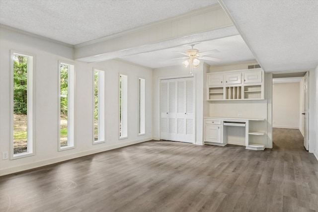 unfurnished living room with ceiling fan, a textured ceiling, built in desk, and wood-type flooring