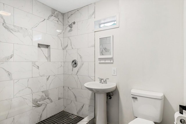 bathroom featuring sink, a tile shower, and toilet