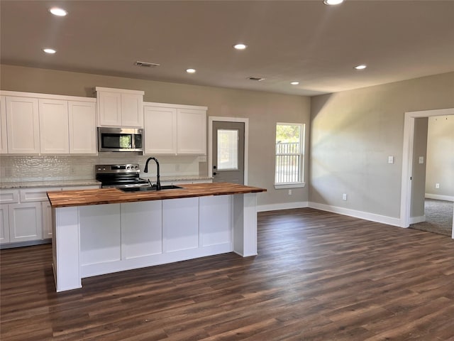 kitchen featuring white cabinets, appliances with stainless steel finishes, a kitchen island with sink, and wooden counters