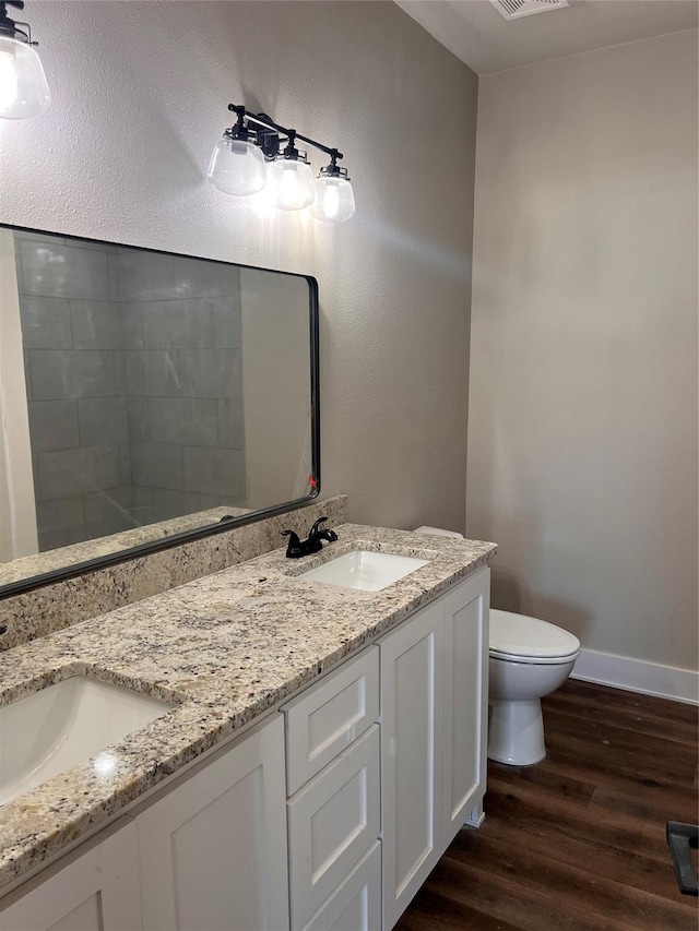 bathroom featuring toilet, double vanity, a sink, and wood finished floors